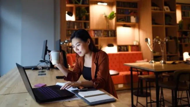 A woman working while holding a cup of coffee